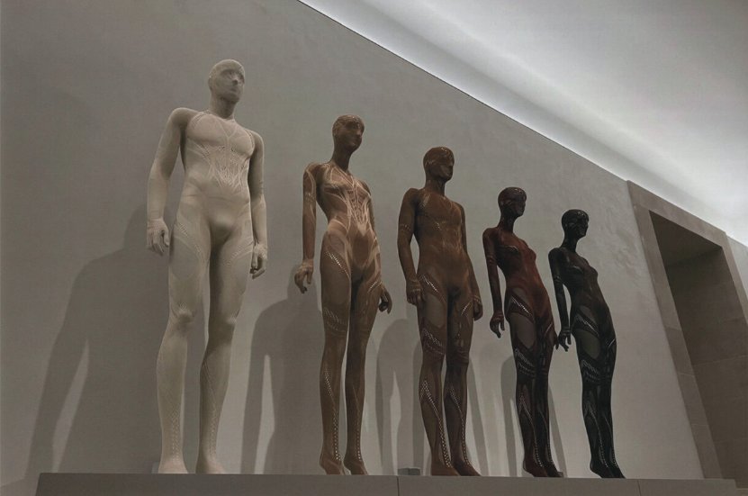 Instalación escultórica de figuras humanas en degradado de tonos de piel, exposición de arte