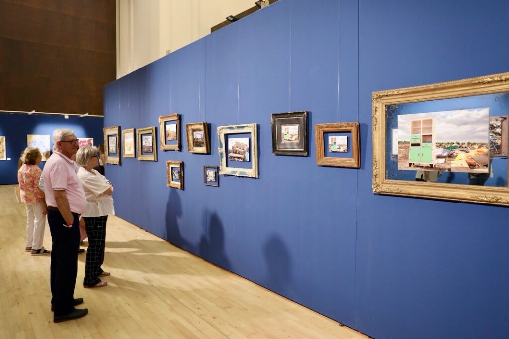 Dos visitantes observan la serie de fotografías con marcos antiguos expuesta sobre paneles azules en San Marcos