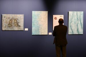 Visitante contemplando las obras de Olga García López y su panel biográfico en el Mes de los Artistas Toledanos de San Marcos